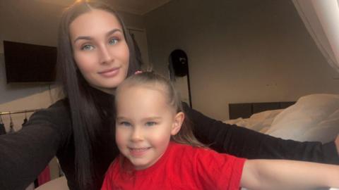 Mother wearing a black top and daughter wearing a red top looking at the camera