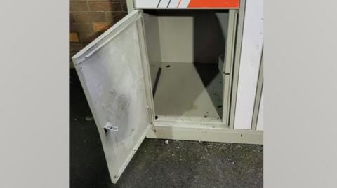 The locker the child climbed into. It is a small grey locker at the bottom of a tower of similar lockers.