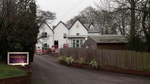Drive leading up to cars home with purple 'Westacre' sign on grass bank.