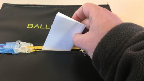 A hand putting a ballot slip in a ballot box