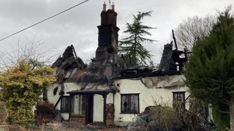 A view of the damaged property. The cottage's roof has been burnt and collapsed while only the chimney part remains.