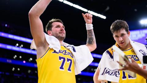 A smiling Luka Doncic celebrates with his arms raised, in the Lakers' yellow vest