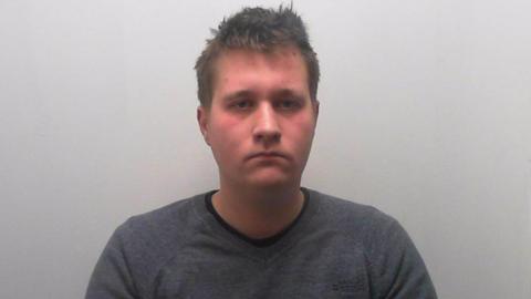 A police image of Adrian Augustyniak with short brown hair and a long-sleeved grey top.