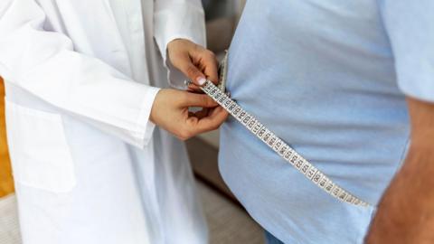 Doctor measures a man's waistline during a clinic check