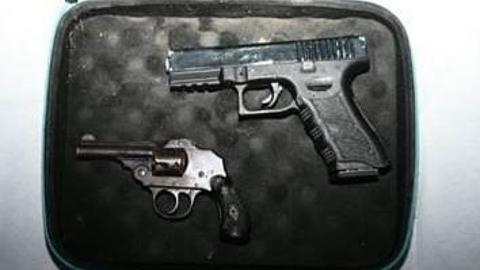 Two guns - a Glock-style pistol and a small vintage-looking enclosed-hammer revolver - lie in a small case which has black padding.