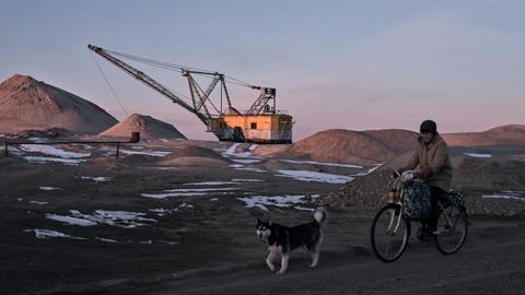 A woman cycles past with her dog as bucket-wheel excavators are at rest at a mine the Zhytomyr region of Ukraine