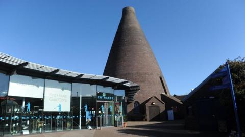 A big cone-shaped brick building, next to a glass building which says 'Red House Glass Cone'