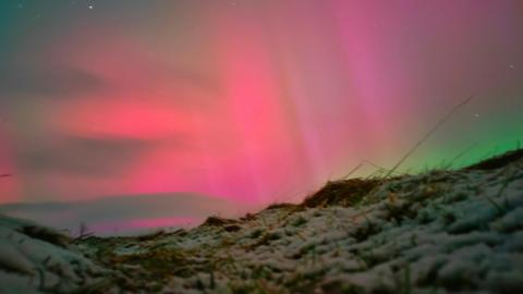 snow covered hill top with bright aurora colours in the sky