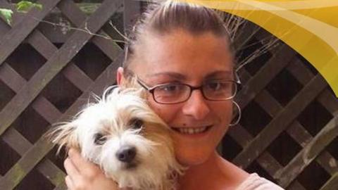 A woman with her hair pulled back had glasses and hoop earrings and is smilig at the camera has she holds a small white dog against her face