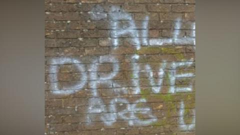 A section of brick wall with graffiti daubed on it in white paint. Only the words "all drive are u" are visible as the image has been cropped.
