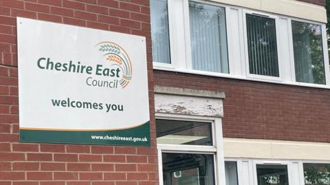 Cheshire East Council's headquarters at Delamere House in Crewe. There is a sign on the building that says Cheshire East Council welcomes you.