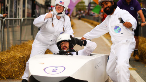 Competitors pose with their soapbox, three people, dressed in white jump suits give the thumbs up to the camera ahead of the race