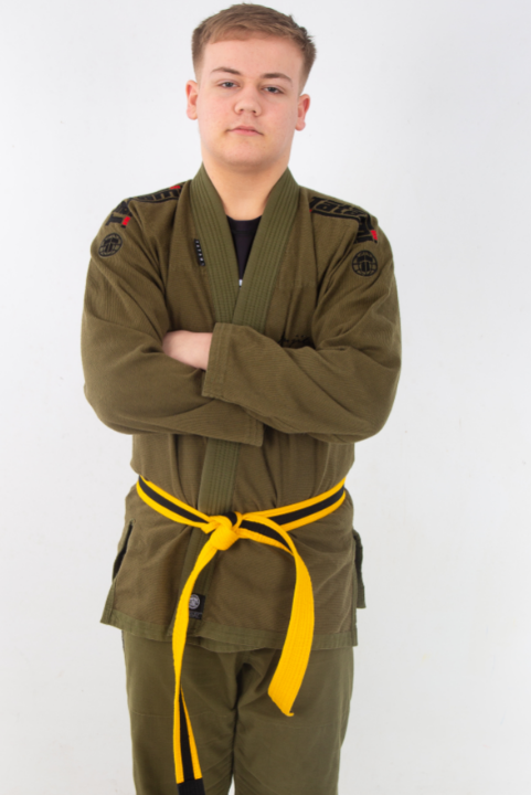 Boy in martial arts clothing. The jacket and trousers are khaki green and his belt is yellow and black. 