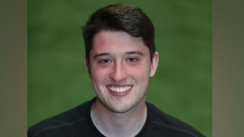 Rhys Williams is a young man with dark hair and he is wearing a dark shirt.