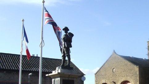 Union and France flags fly on either side of the sculpture of a World War One soldier in Carnforth