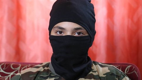 A 13-year-old boy who wishes to be named 'Abu Hattab' sits wearing a black balaclava