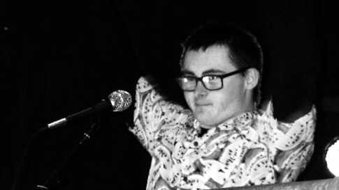 A black and white image shows Finley with his arms up in the air as he stands in front of a microphone. 