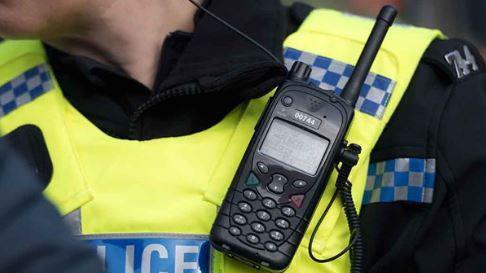 A close-up of a police officer. The picture shows the upper part of the officer's body, with a police radio attached.