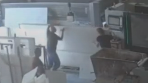 A still of CCTV footage that shows two men trying to hold up a large white slab of stone. Another man watches on moments before it falls