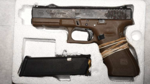 A semi-automatic handgun in a polystyrene case with a brown handle and elastic bands wrapped around the grip, and a black ammunition clip with a bullet visible at the top