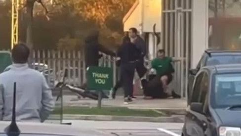 Three youths dressed in black appear to be scuffling with a Subway worker wearing a green uniform outside a retail unit. A bicycle is on the ground behind one of the youths.