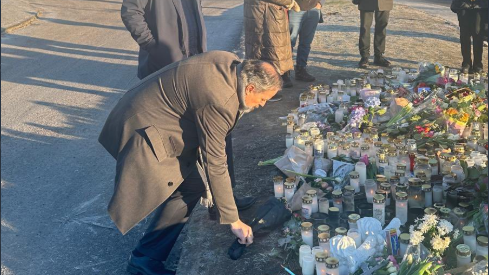 Bojan Sosic stoops to lay flowers on the ground beside other flowers and candles