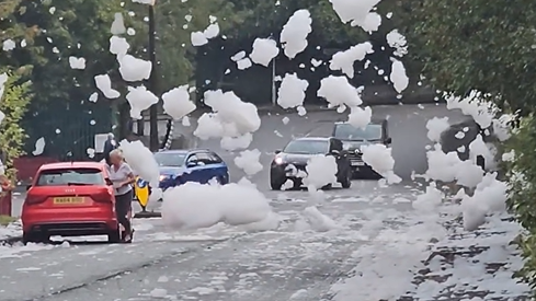 Huge white bubbles drift among traffic and a parked red car