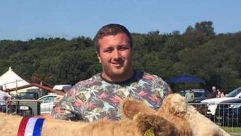 Liam is pictured here with one of his cows at an agricultural show. Liam is wearing a multicoloured t-shirt and has short blonde/brown hair.