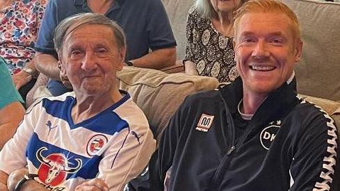 Rod Thornhill, sat with crossed arms and wearing a blue and white hooped Reading FC home shirt and grey hair, sat next to Dave Kitson, who has ginger hair and a black training top with "DK" embossed on it 