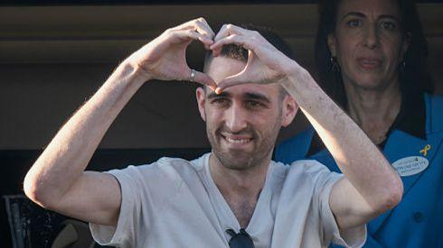 A man in a grey T-shirt and sunglasses holds his hands in a heard position.