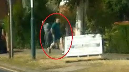 A very low quality image of a man running or walking down a street wearing a green T-shirt and shorts.