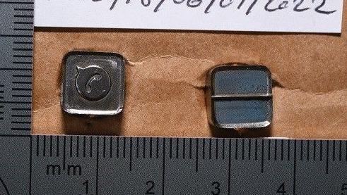 Two small metal stamps, about a centimetre wide each, next to rulers in an police investigation picture.