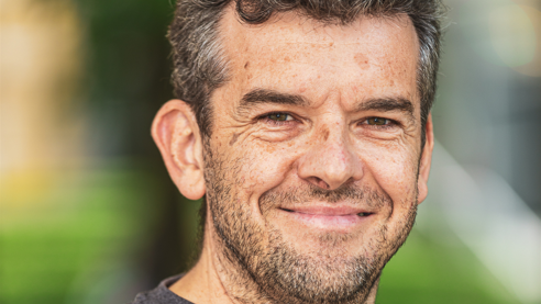 Christy is smiling to the camera in this close-up phot. He has dark hair and a short beard.