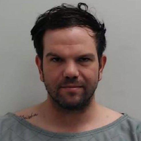 A mugshot of a man with short brown hair in a grey top