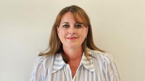 A head and shoulders image of a woman with shoulder-length light brown hair, smiling at the camera and wearing a white and blue stripped casual shirt style top.
