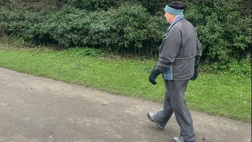 Derrick Downs wearing fleece and woolly hat and gloves, walking on a path away from camera 