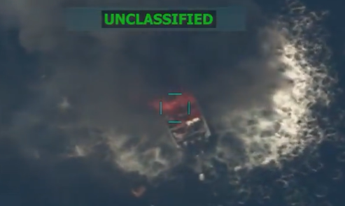A still from a surveillance video showing a boat in the ocean with smoke and fire coming off of it. It says unclassified in neon green all-capped letters.