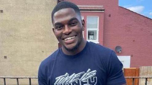 Chris Kaba smiling, standing in front of a garden fence