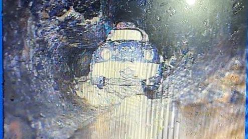 The toy car pictured in a drain. It appears to be a blue and white plastic car and is sitting in sludge.