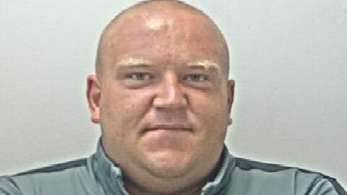 Police mugshot of shaven headed John Robinson, wearing a light blue and navy tracksuit.