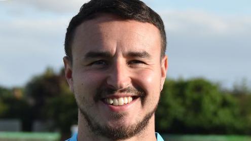 A picture of James Hitchcock, a man with short brown hair and stubble. He is wearing a light blue football jersey.