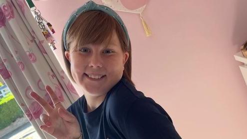 Eve Shipley is pictured making a "peace" sign with her hand. She is in a pink-painted room and is smiling at the camera.