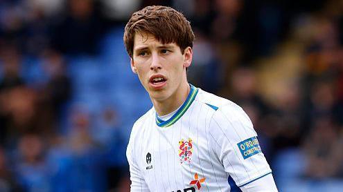 Stephan Negru standing on the pitch wearing Tranmere kit, holding his arms out to his side with his palms facing upwards