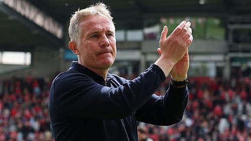 Phil Parkinson applauds as he is filmed by a TV camera 