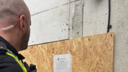 A police officer looks at the closure order on chipboard at the house.