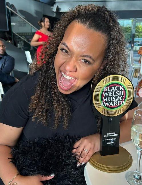 Lily Beau holding her Best New Artist award and celebrating at a table