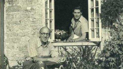 A black and white image of Norman Notley and David Brynley at the window of their stone cottage