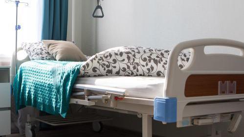 A bed in a care home. There are blankets and a couple of cushions on top of it.