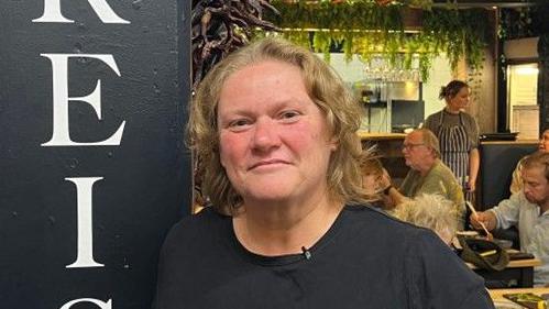 Natalie Jenkins stands in her restaurant with guests eating in the background