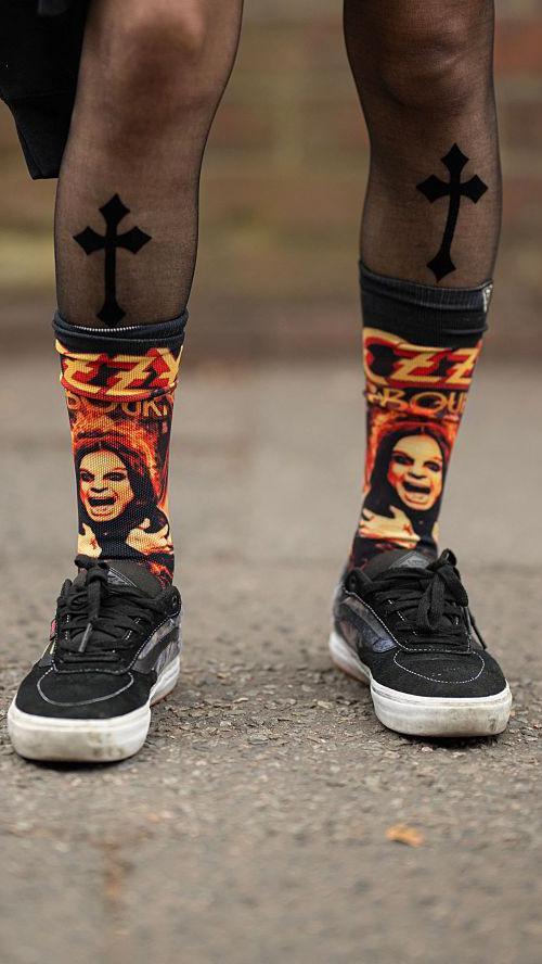 A close-up of a person's lower legs and feet. They are wearing black trainers, and black and orange socks with Ozzy Osbourne's face on them.